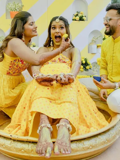 A playful moment where the bride is fed a laddoo during her Haldi ceremony. It's all about fun, family, and food.