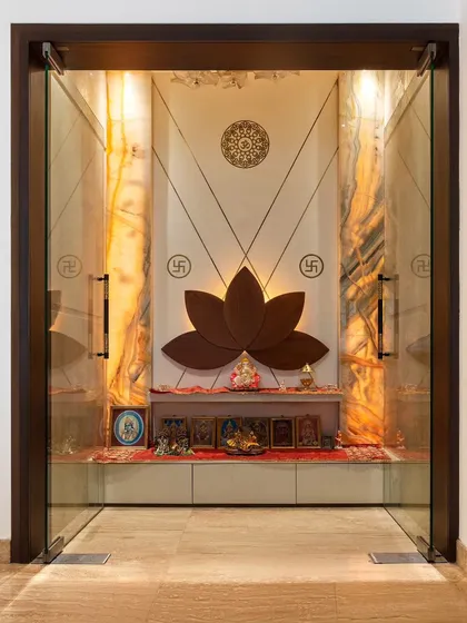 We reinvent traditional spaces with a contemporary lens. This pooja room features a custom-carved teak wood lotus as a serene backdrop, flanked by glowing backlit onyx marble and accented with brass inlays, creating a space that is both modern and deeply reverent.