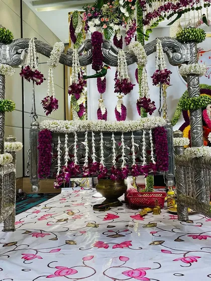 A close-up of the ornate silver-plated cradle, or 'thottil', decorated with delicate garlands of jasmine and purple flowers. This is a central part of a traditional Hindu naming ceremony, and we ensure it is beautifully presented.