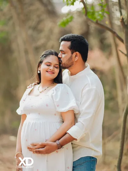 An intimate outdoor portrait with the partner kissing the mother-to-be's forehead.