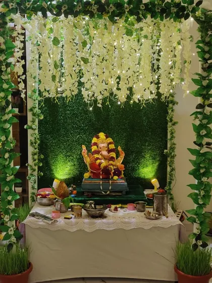 This decor creates a magical, forest-like grotto for Ganpati, using a green backdrop and a ceiling of hanging flowers and lights.