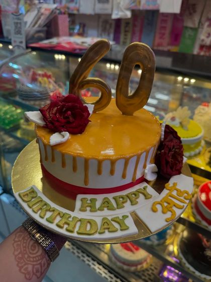 An elegant cake for a 60th birthday. The design features a rich caramel drip, red roses, and golden numbers, creating a sophisticated and celebratory look for this important milestone.