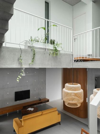 The living area is defined by its raw, minimalist material palette, including an exposed concrete feature wall and ceiling. The yellow sofa adds a vibrant splash of color to the neutral space.