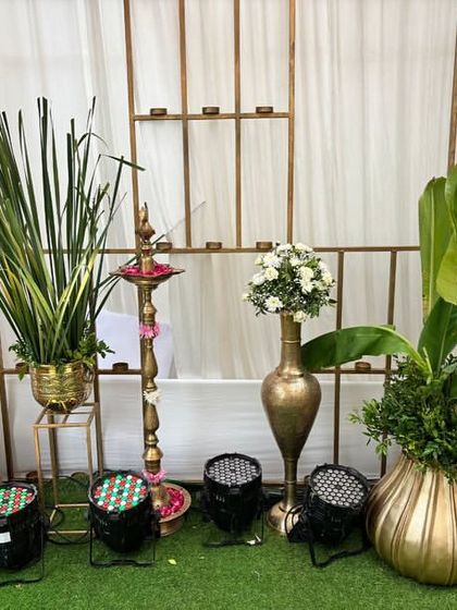 A mix of modern and traditional decor, with tall greenery in golden pots, a classic brass lamp, and banana leaves, all beautifully lit.