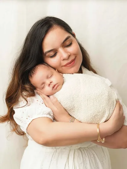 A mother holds her swaddled newborn, her expression serene and loving. The soft, white-on-white styling creates an angelic and timeless portrait.