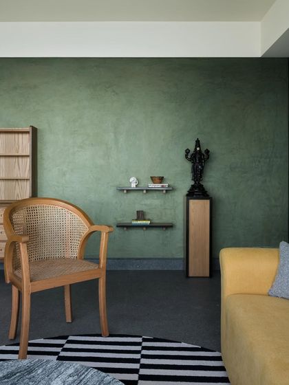 A living room corner featuring a caned armchair and a portion of a yellow sofa. I use natural materials like cane and wood to add texture and warmth, creating a sanctuary from the city outside.