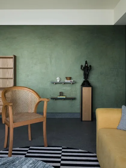 A living room corner featuring a caned armchair and a portion of a yellow sofa. I use natural materials like cane and wood to add texture and warmth, creating a sanctuary from the city outside.
