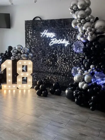 An 18th birthday party setup with a black shimmer wall, a black and silver balloon arrangement, and bold marquee numbers.