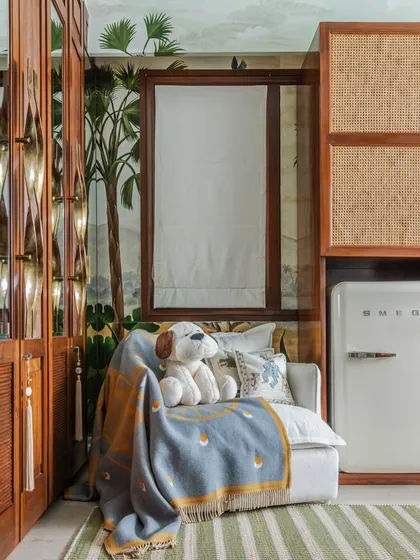 I always include a cozy corner for mom and baby. This little nook features a comfortable armchair, soft blankets, and a mini-fridge, all set against the backdrop of the jungle mural and warm rattan furniture.