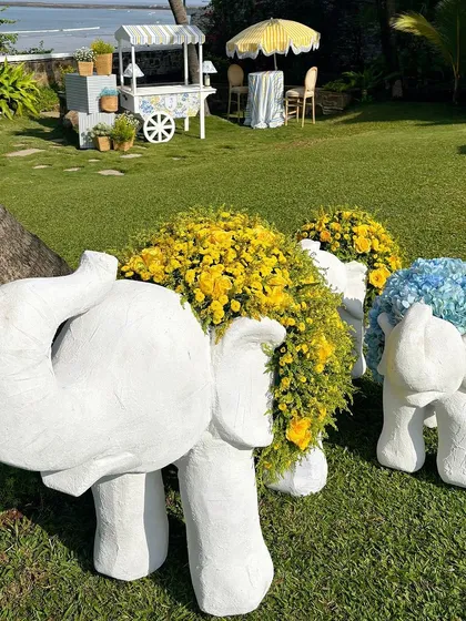 A beautiful outdoor setup for a baby mundan ceremony, featuring elephant statues adorned with yellow and blue flowers.