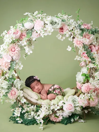 A wider angle of our popular floral hoop setup, showing a newborn sleeping peacefully inside a large ring of pink and white flowers against a soft green backdrop.