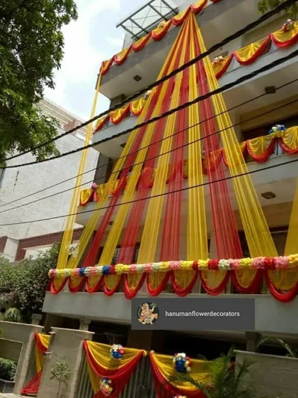 I make sure the festive feeling starts right at the entrance. This is an exterior decoration for a multi-story residence, using bright yellow and red drapes and floral arrangements to make the entire building look ready for a celebration.