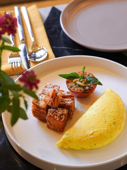 A perfectly folded French omelette made with organic eggs, served with crispy potato hash and a basil-topped grilled tomato. It's a simple, elegant, and delicious breakfast choice.