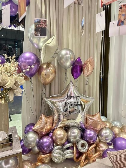 A beautiful balloon bouquet in metallic shades of purple, silver, and gold. A large star-shaped foil balloon with a custom "Happy Birthday" message serves as the centerpiece.