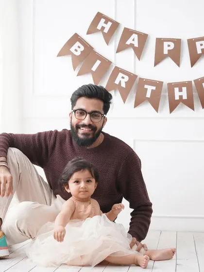 A sweet father-daughter portrait taken during a first birthday session, with a 'Happy Birthday' banner in the background.
