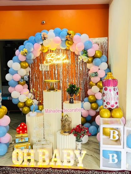A "He or She" gender reveal or baby shower theme. This setup uses a pink and blue balloon arch, 'OH BABY' light-up letters, and baby bottle foil balloons to create a fun and festive atmosphere.