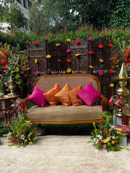 A vibrant Mehandi ki Mehfil, styled for a modern celebration while honoring tradition. This outdoor setup features a beautiful carved wooden screen, marigold garlands, and plush seating in jewel tones, creating the perfect backdrop for photos and festivities.