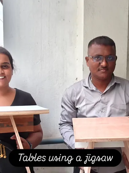 Two students proudly holding the tables they built using a jigsaw for the curved legs. This is a great example of how to incorporate design elements into a simple project.