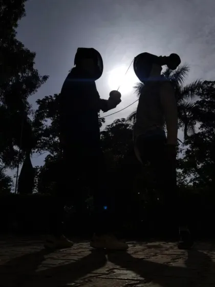 The moment before a bout begins, two fencers face each other, their concentration captured in this striking silhouette against the sun.