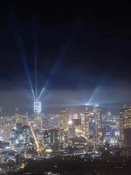 A wide shot of the Mumbai skyline at night, with spotlights from skyscrapers cutting through low-hanging clouds.