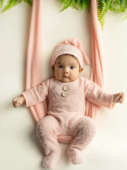 A sweet and simple portrait of the baby in a soft pink outfit and matching hat, looking directly at the camera.