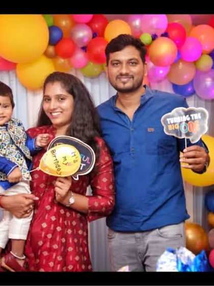 A family holds fun photo props while posing in front of a vibrant balloon backdrop at a birthday party.