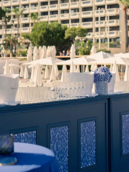 The sleek blue and white bar setup for the welcome event, with a backdrop of beach umbrellas and the sparkling Mediterranean.