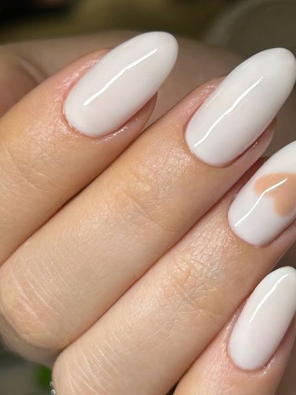 A sweet and simple design featuring milky white nails with a single, delicate nude heart accent on the ring finger. A perfect example of minimalist nail art.