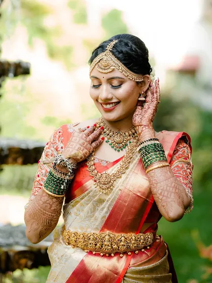 A beautiful portrait of our smiling bride. Her complete temple jewellery set, with its layers and detailed carvings, perfectly complements her cream and red bridal saree.