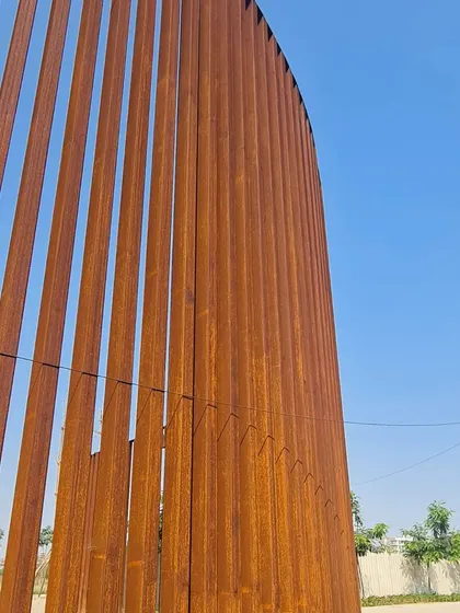 An upward-looking view of the Corten steel screen, emphasizing its height and the graceful curve of its form.