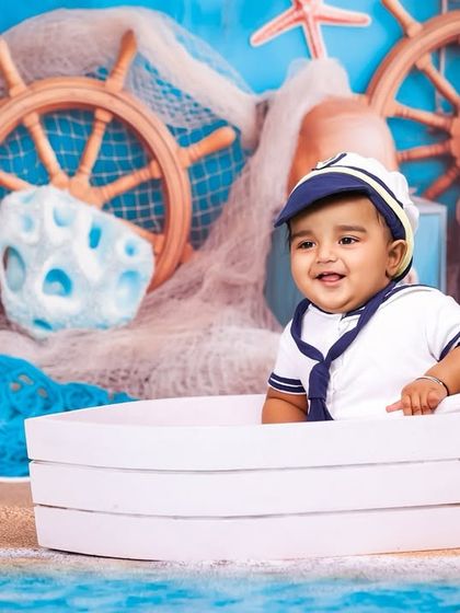 A happy sailor enjoying the sea. The bright blue backdrop and detailed props create a convincing and fun maritime scene for this baby boy's photoshoot.