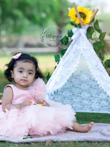 A one-year-old girl in a pink dress, sitting in front of our boho teepee setup.