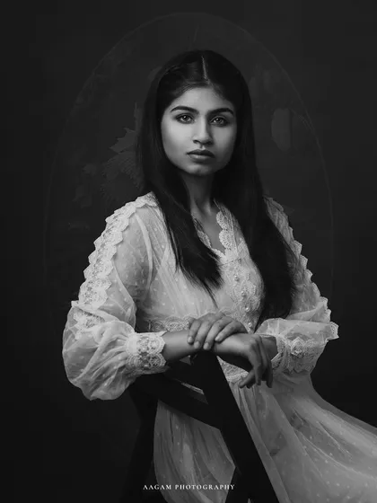A classic black and white portrait of a "muse" in a delicate lace dress. The dark background and soft lighting create a timeless, painterly feel.