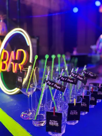 A vibrant neon-themed bar setup, complete with a glowing 'BAR' sign and personalized drink tags for 'Raj & Pooja's Neon Night'.