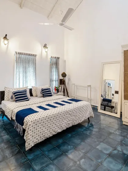 Another view of the blue-and-white bedroom, showing the full-length mirror and spacious layout. The high ceiling and light colors make the room feel open and serene.