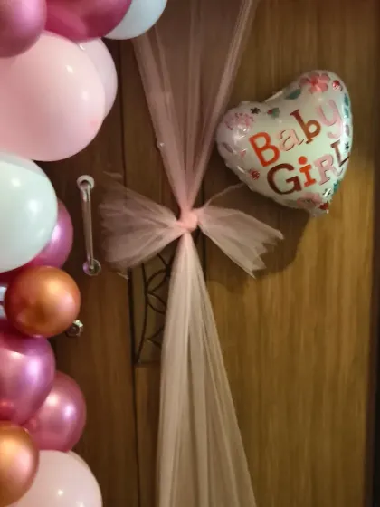 An elegant door decoration for a baby girl's welcome, featuring a pink tulle bow, a heart-shaped foil balloon, and a cascade of pink and chrome balloons.