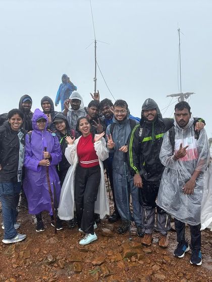 Braving the rain and mist together. A group of trekkers, clad in ponchos, stands proudly at the summit. Moments like these, facing the elements as a team, are what forge the strongest bonds.