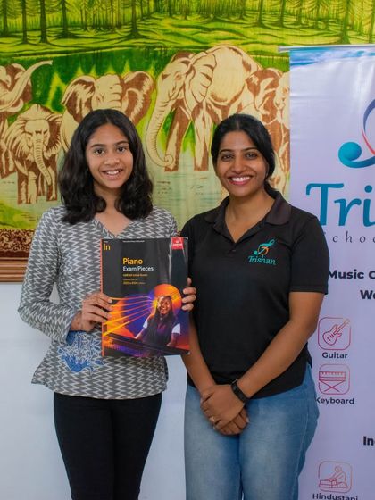 A student holding her ABRSM piano exam book with her teacher.