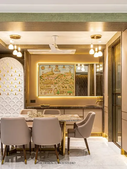 This dining area is a beautiful example of modern Indian design. The space features a marble-top table, plush beige chairs, and a stunning piece of traditional art that is highlighted with concealed lighting.