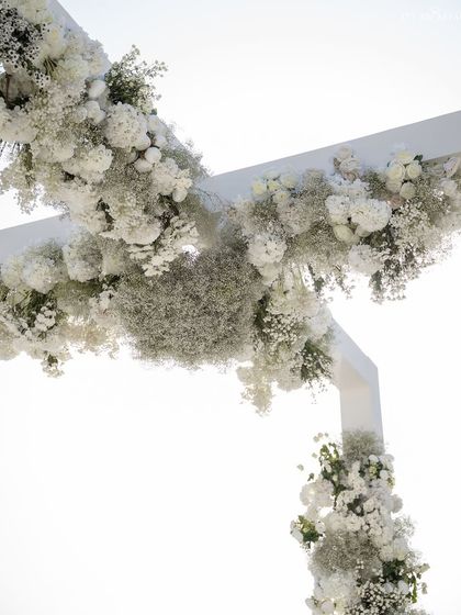 A close-up of the floral arrangement on the mandap arch. A dense cloud of white hydrangeas and baby's breath creates a soft, ethereal texture against the bright sky.