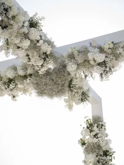 A close-up of the floral arrangement on the mandap arch. A dense cloud of white hydrangeas and baby's breath creates a soft, ethereal texture against the bright sky.