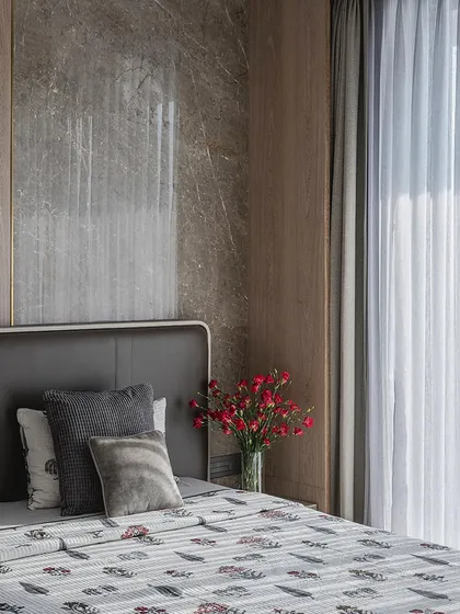 A detail shot of the bedside in a neutral-toned bedroom, showing the mix of textures between the marble wall, wood paneling, and soft bedding.