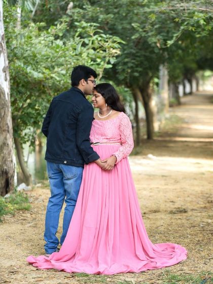 A romantic couple portrait on a park path. The dad-to-be kisses his partner's forehead as she smiles in her pink gown.
