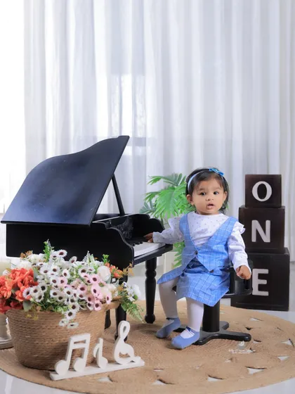 A vertical composition of the piano-themed first birthday shoot, perfect for capturing the full scene from the "ONE" blocks to the little girl's curious expression.