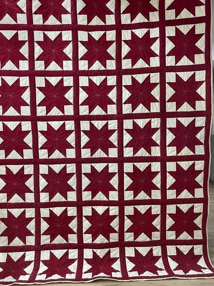 A bold and graphic quilt featuring a repeating red star pattern against a white background.