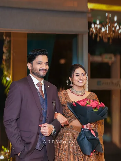 The couple making their grand entrance, holding a bouquet of red roses, their smiles lighting up the room.