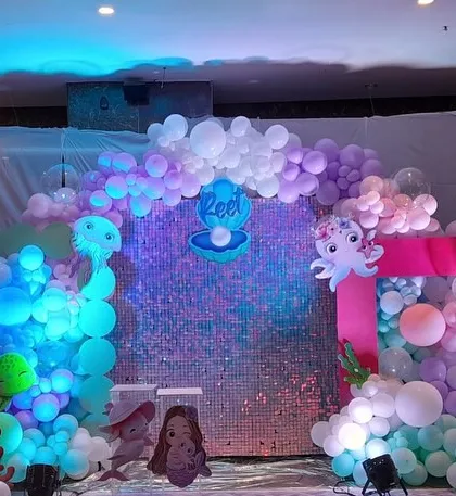 An enchanting underwater theme for a baby welcoming party. The decor features a shimmering sequin wall, mermaid and sea creature cutouts, and a pastel balloon wave.
