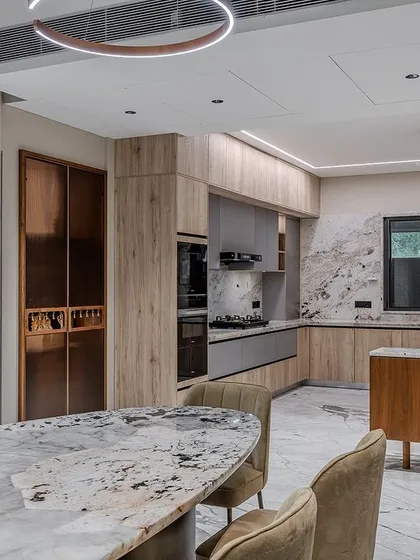 The kitchen is designed as part of an open-plan living and dining area, with the materials and colors of the kitchen complementing the dining furniture for a cohesive design.