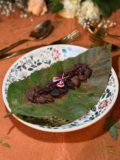 An earthy and artistic presentation of a dish served on a large leaf over a patterned plate. The edible flower garnish adds a pop of colour, highlighting our use of natural elements in plating.