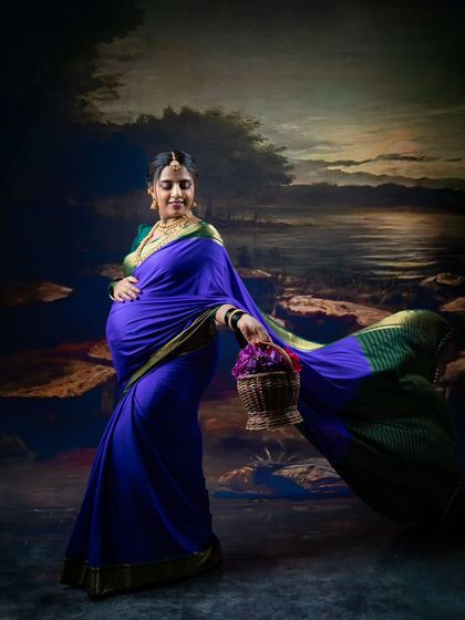 A graceful portrait of a pregnant woman in a flowing purple saree, holding a basket of flowers against a painterly backdrop.